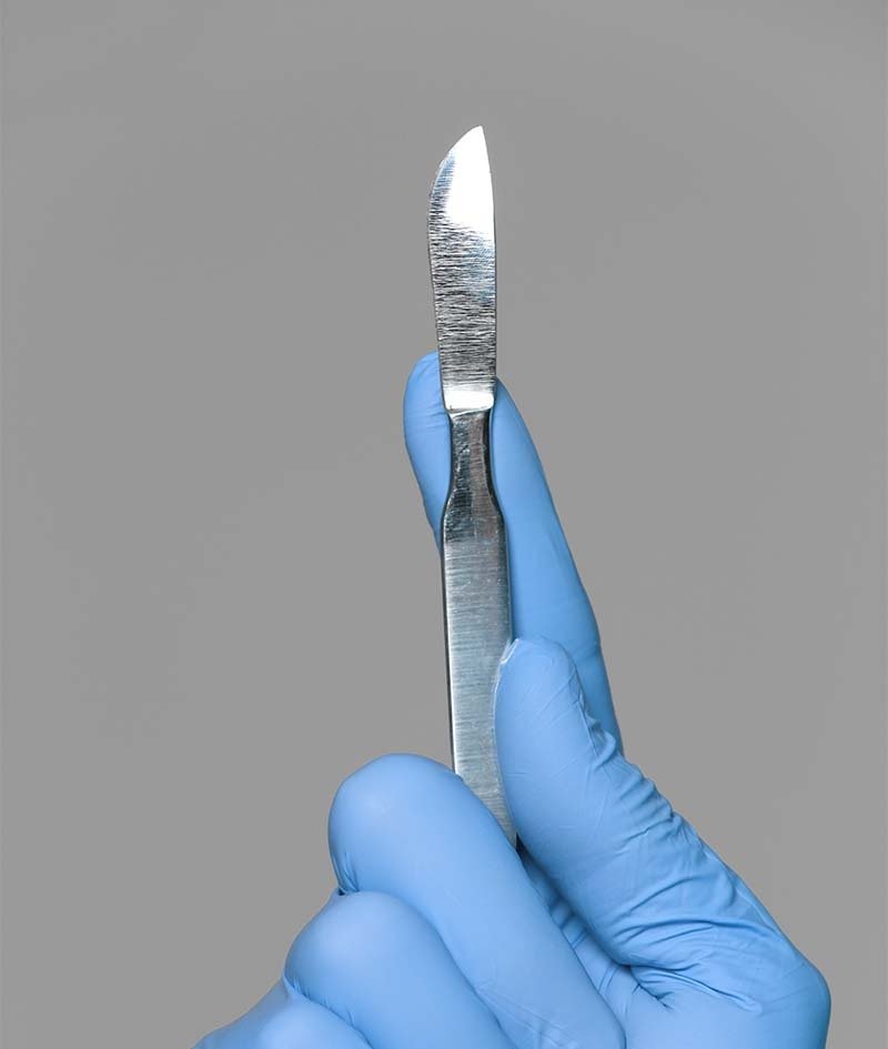 A scalpel held in a gloved hand
